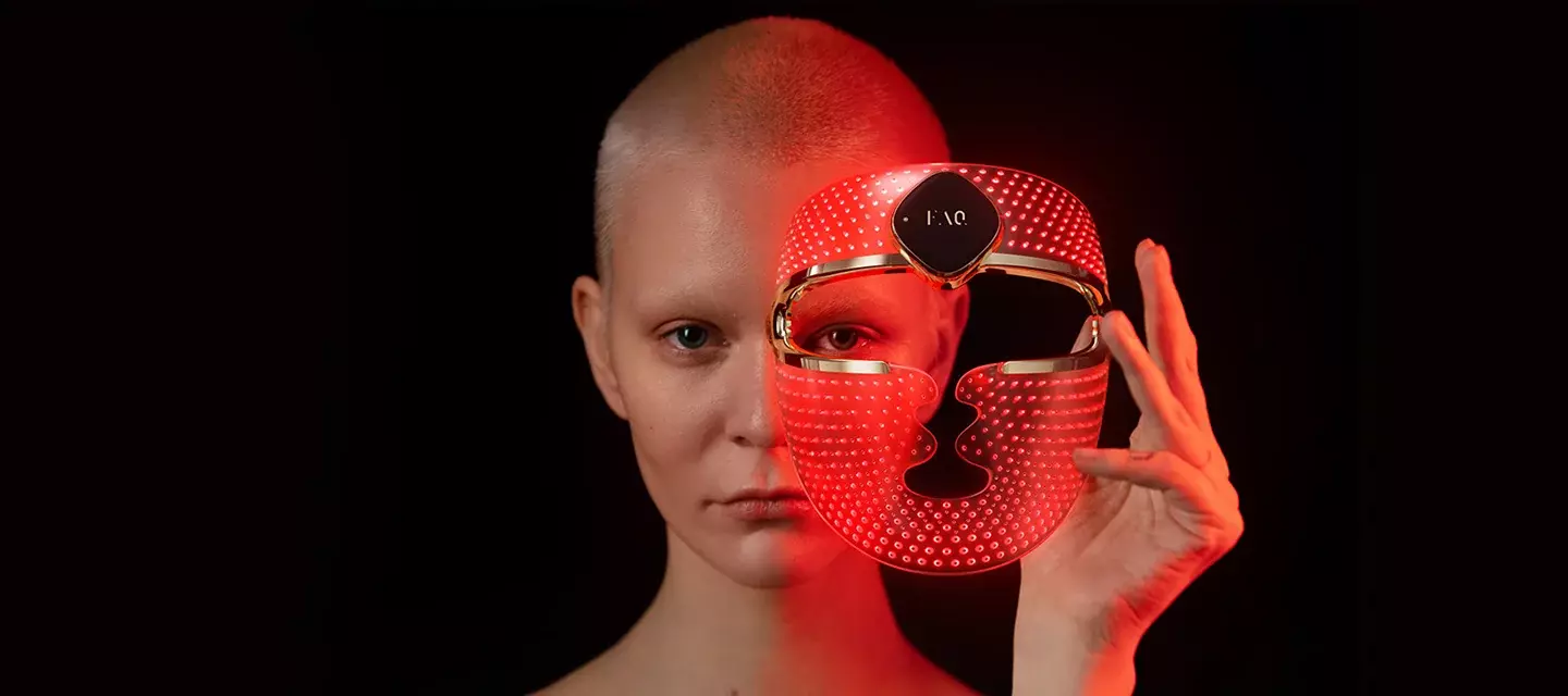Androgynous beautiful young woman with short hair putting on FAQ 202 red light therapy mask